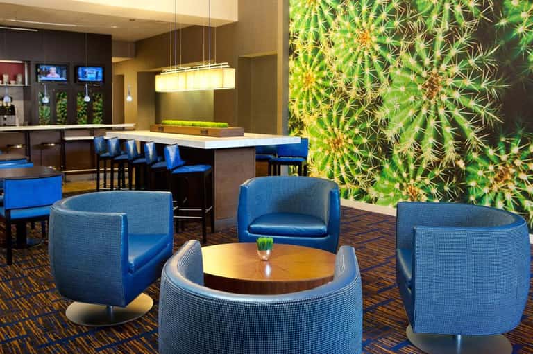 Modern hotel lounge with blue accent chairs, green living wall, bar counter, and contemporary design