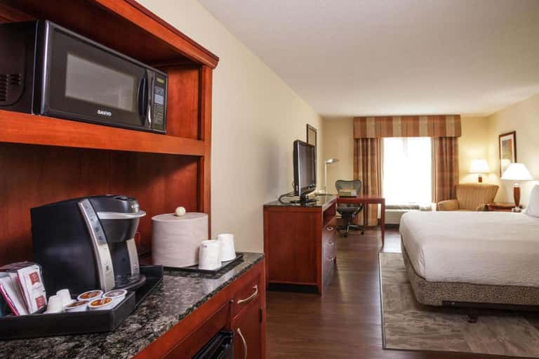 Hotel room interior with queen bed, wood furnishings, coffee maker, and modern amenities