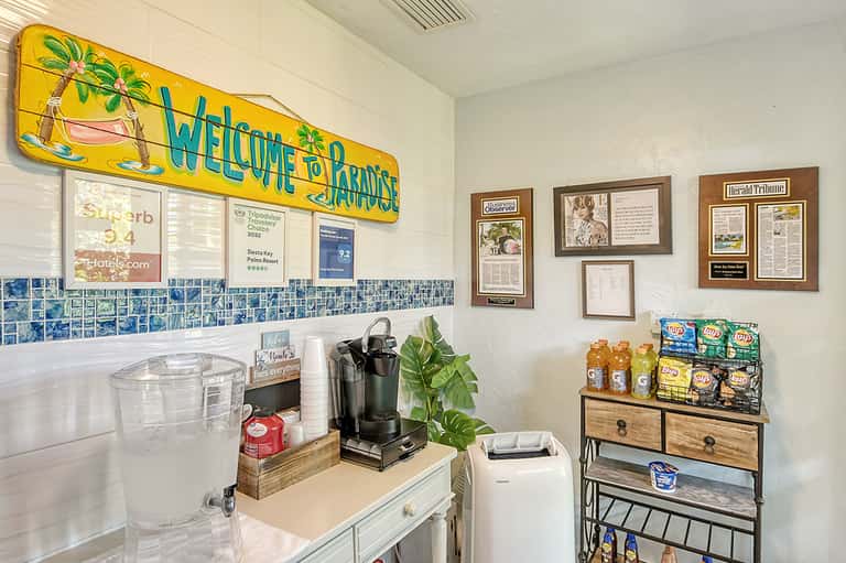 Hotel welcome desk with yellow 'Welcome to Paradise' sign, white cabinetry, coffee maker, and informational displays