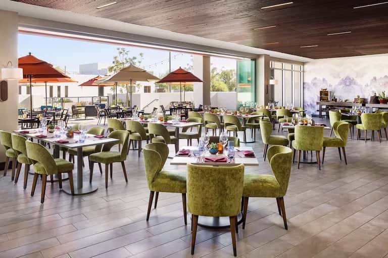 Contemporary restaurant dining room with green chairs, white tables, umbrellas, and outdoor terrace view