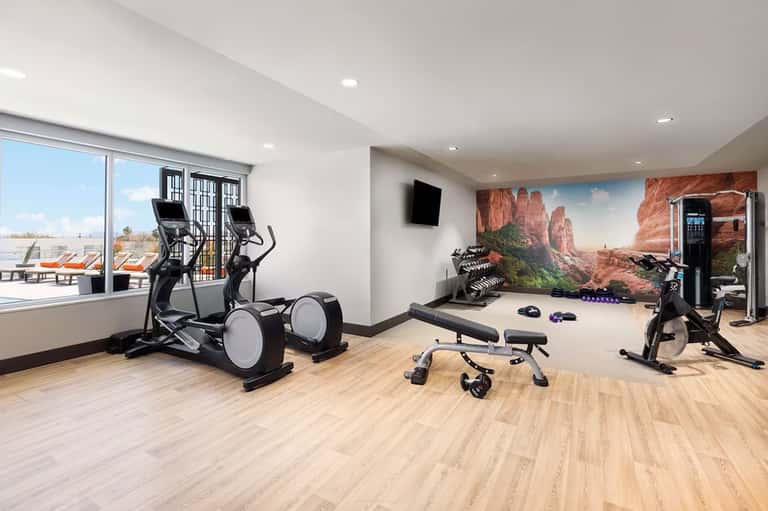 Modern fitness center with elliptical machines, stationary bikes, weights, and desert landscape mural