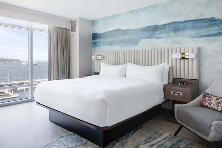 Waterfront hotel room with white bed, striped headboard, ocean view, and contemporary furnishings