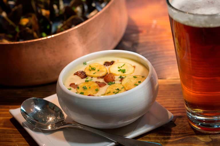 Creamy potato soup with bacon bits and beer on table
