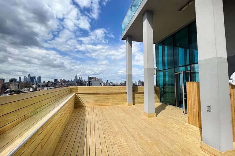 Wooden rooftop deck with city skyline view, modern glass doors, and white columns