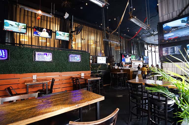 Modern sports bar interior with wooden tables, neon signs, and TV screens