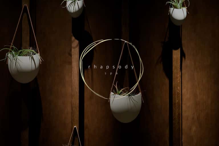 Minimalist spa entrance with hanging white planters and Rhapsody spa signage