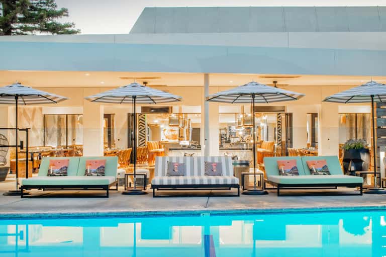 Modern pool area with turquoise umbrellas, colorful lounge seating, glass building, and contemporary design