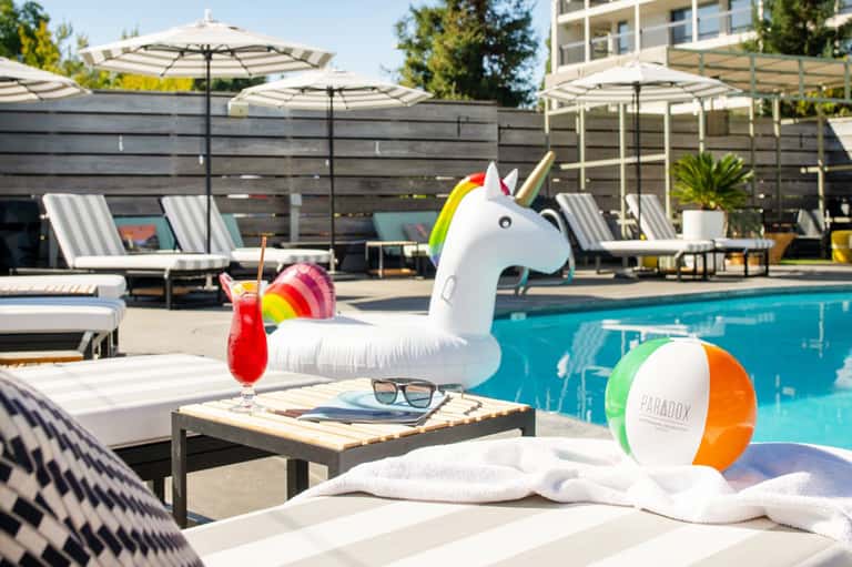 Resort pool area with unicorn float, lounge chairs, umbrellas, and colorful drinks
