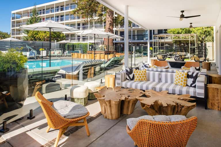 Modern resort patio with wooden accent tables, striped seating, and view of pool beyond