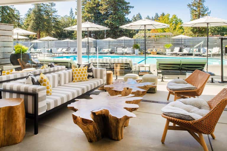 Modern pool lounge with striped seating, wood accents, umbrellas, glass fencing, and pool view