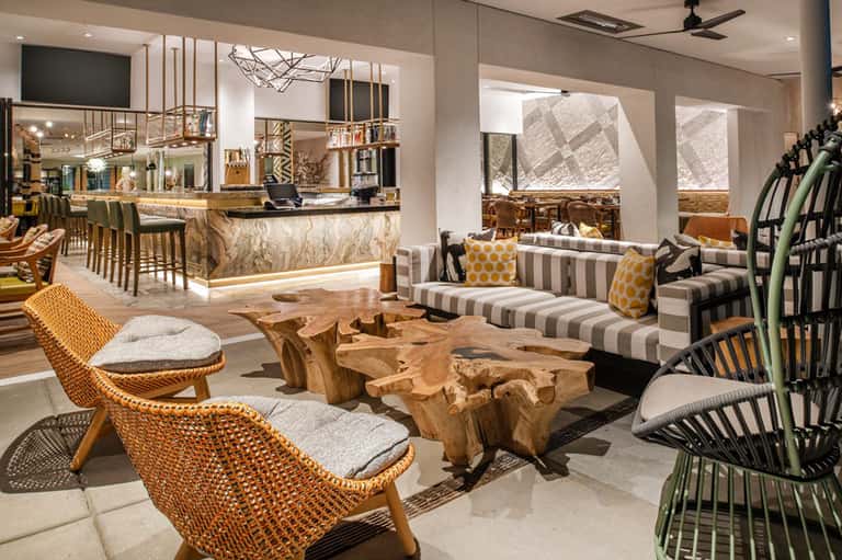 Contemporary resort lounge with woven chairs, striped sofa, and marble bar