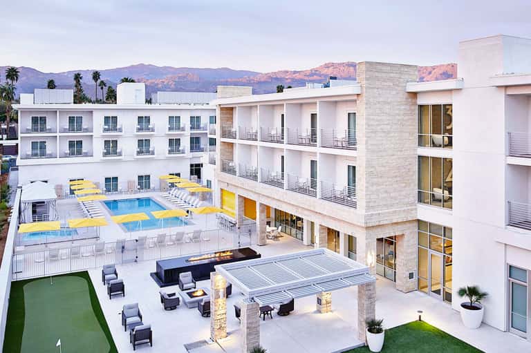 Modern white hotel building with yellow lounge chairs by pool and mountain backdrop
