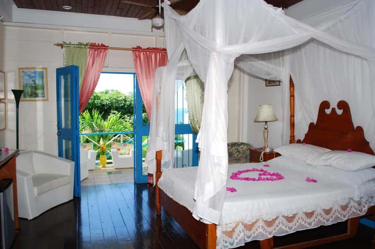 Tropical bedroom with canopy bed, blue doors opening to ocean view balcony