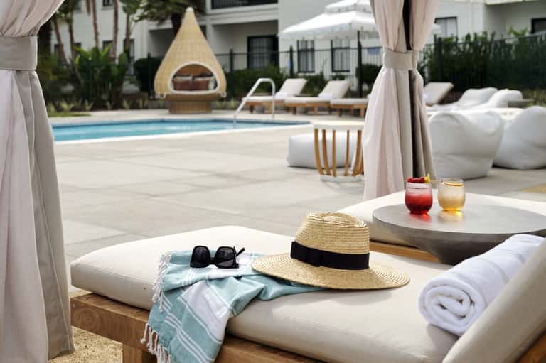 Luxury poolside lounge with cabanas, white furnishings, and teepee-shaped day bed structure