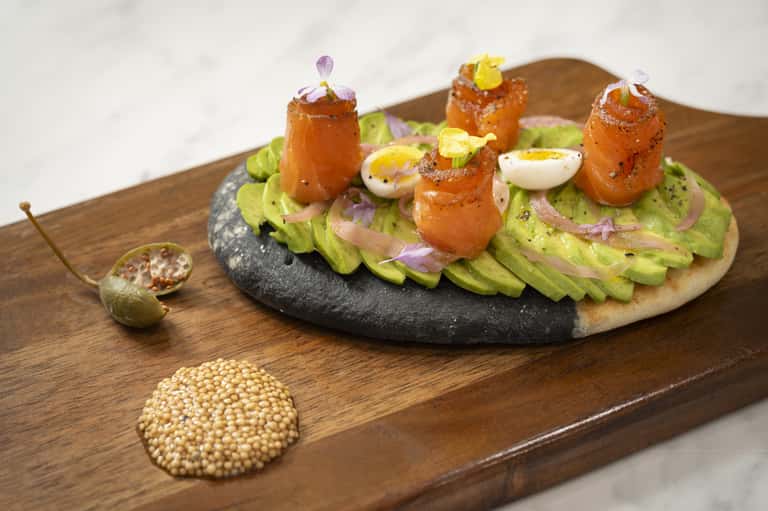 Gourmet appetizer plate with avocado spread, prawns, and edible flowers on wooden board