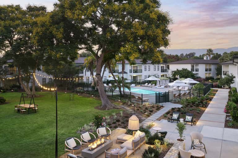 Resort courtyard at dusk with pool, fire pit seating, string lights, and manicured lawns