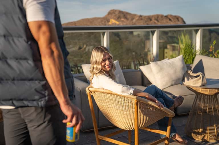Woman smiling on wicker lounge chair on desert hillside terrace with mountain views