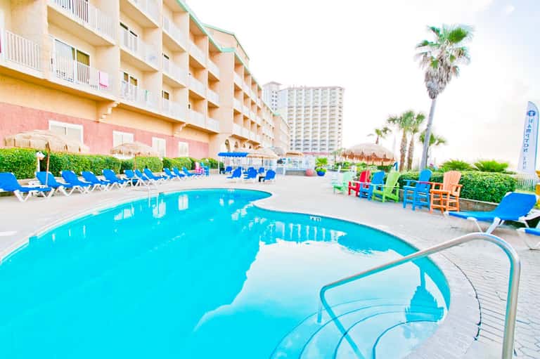 Bright turquoise swimming pool with lounge chairs and palm trees at beachfront resort