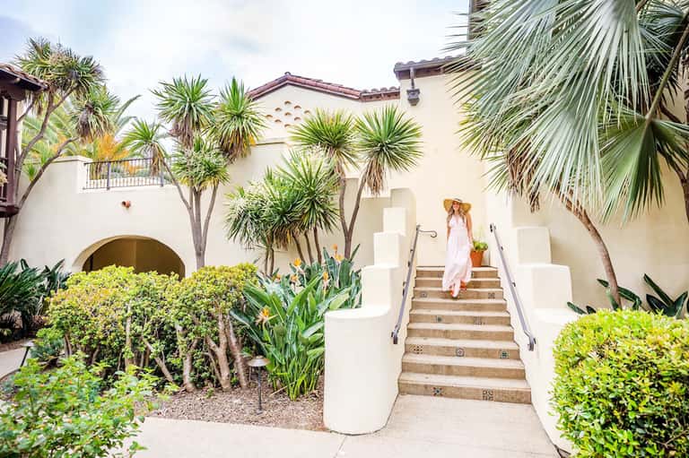 Spanish-style resort courtyard with white staircase, palm trees, and arched architectural details