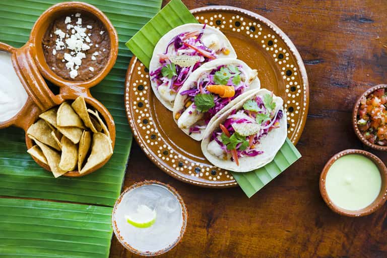 Traditional tacos with purple cabbage slaw, chips, salsa, and lime served on decorative wooden plates