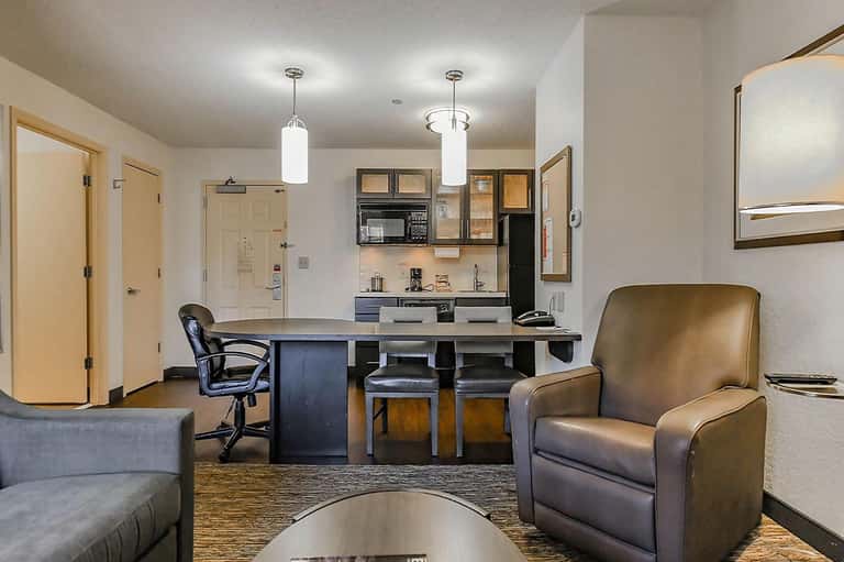 Modern hotel suite kitchenette with dark cabinetry, seating area, and contemporary furnishings
