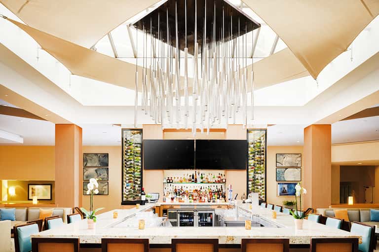 Modern bar with brass chandelier, lounge seating, and illuminated ceiling elements