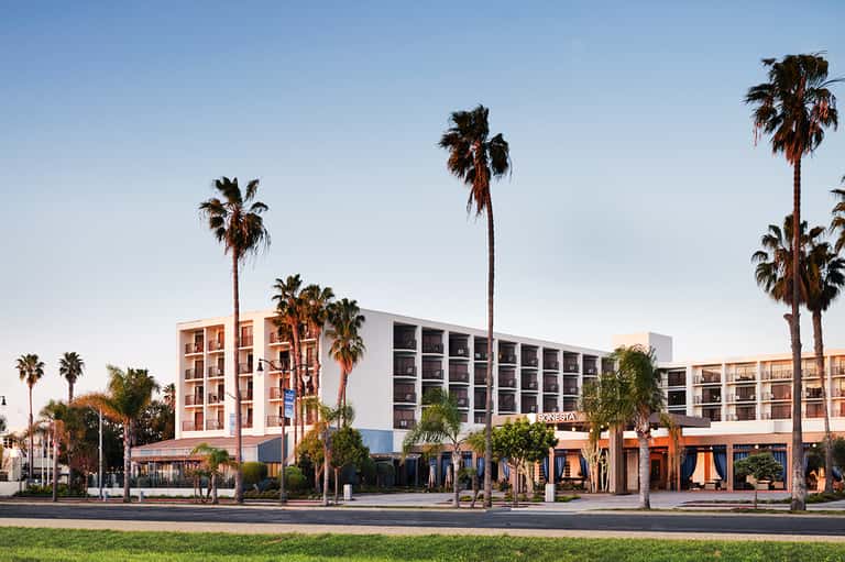 Modern beachfront resort building with palm trees, colorful facade, and ground-floor shops