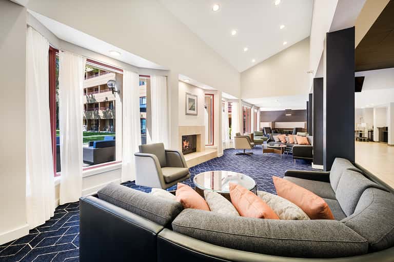 Contemporary hotel lobby lounge with curved seating, fireplace, and large windows