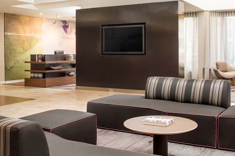 Modern hotel suite with dark accent wall, TV, striped sofa, low tables, and contemporary furnishings
