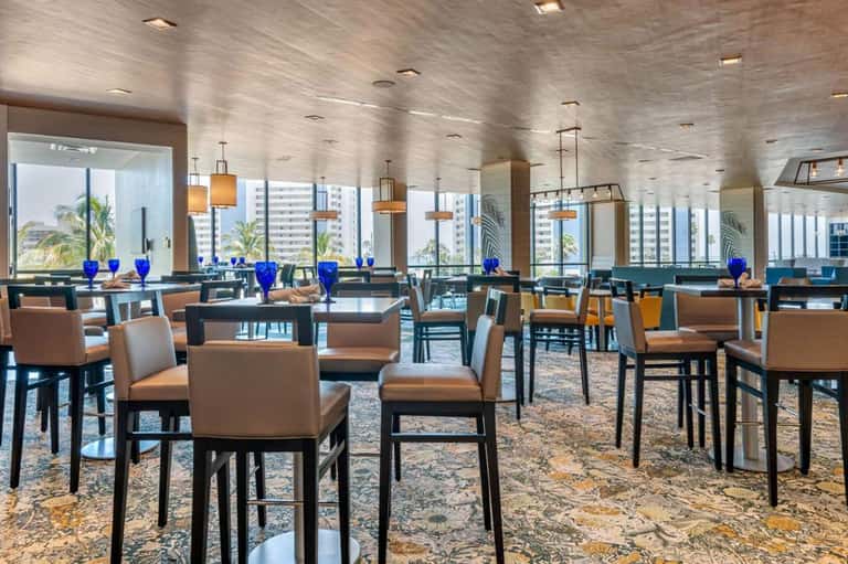 Upscale dining lounge with high-rise windows, blue glassware, modern chairs, and city views
