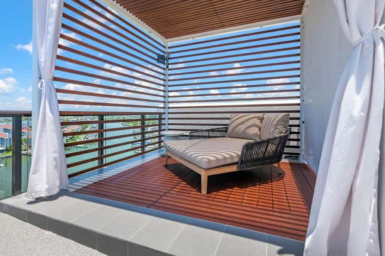 Modern balcony lounge with striped privacy screen, daybed, and water views