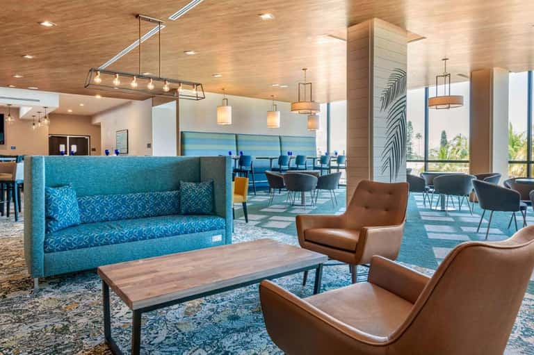 Modern resort lobby with turquoise seating, wood ceiling, pendant lights, and floor-to-ceiling windows