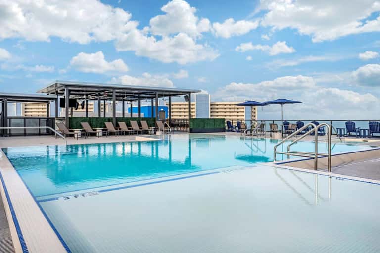 Resort pool deck with swimming pools, covered cabanas, and beachfront views under clear blue sky