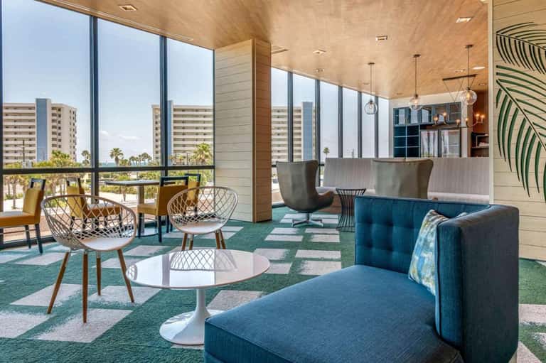 Modern hotel lounge with floor-to-ceiling windows, hanging lights, and coastal views