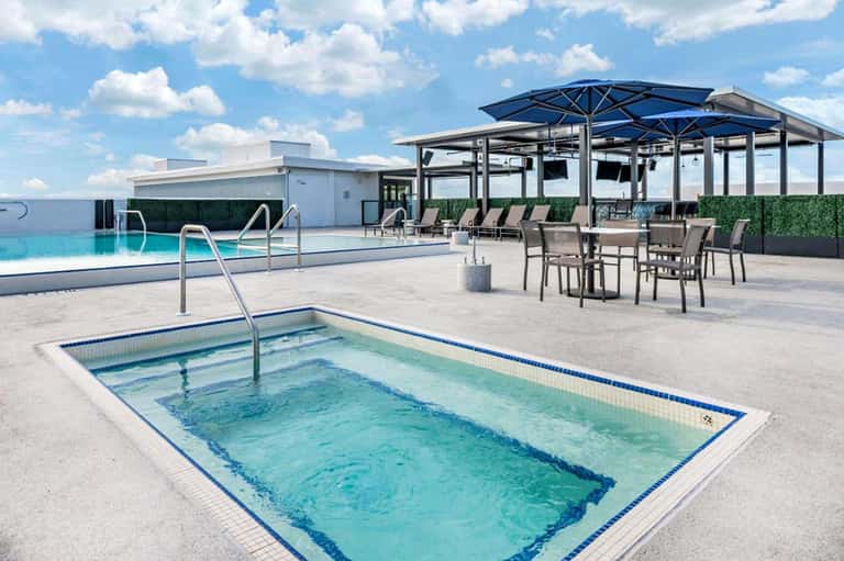 Resort rooftop area with spa pool, lounge seating, umbrellas, and modern building architecture