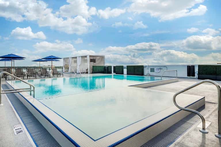 Modern rooftop pool with umbrellas and lounge seating overlooking flat landscape