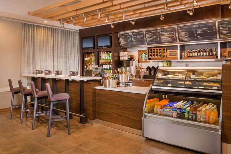 Upscale coffee shop interior with wooden beams, bar seating, menu boards, and display cases with pastries