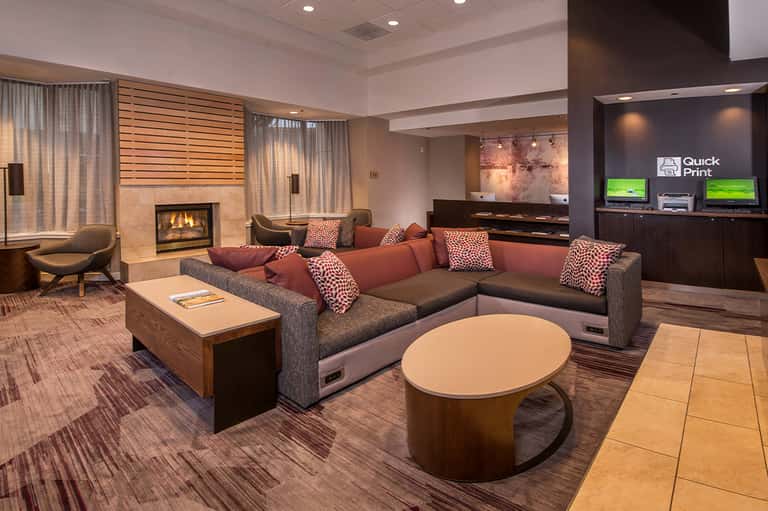 Modern hotel lobby lounge with fireplace, sectional sofa, and Quick Print service area