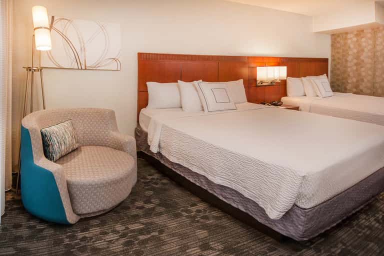 Modern hotel room with two queen beds, orange headboard, and contemporary furnishings