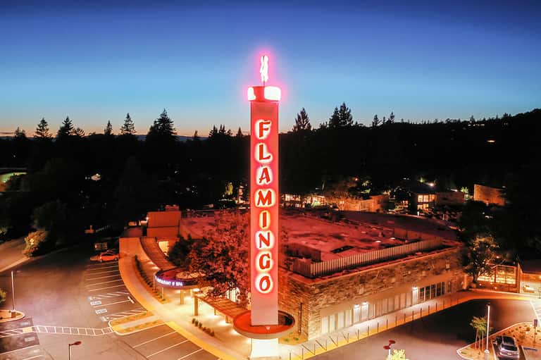 Illuminated red Flamingo neon sign at dusk with resort buildings