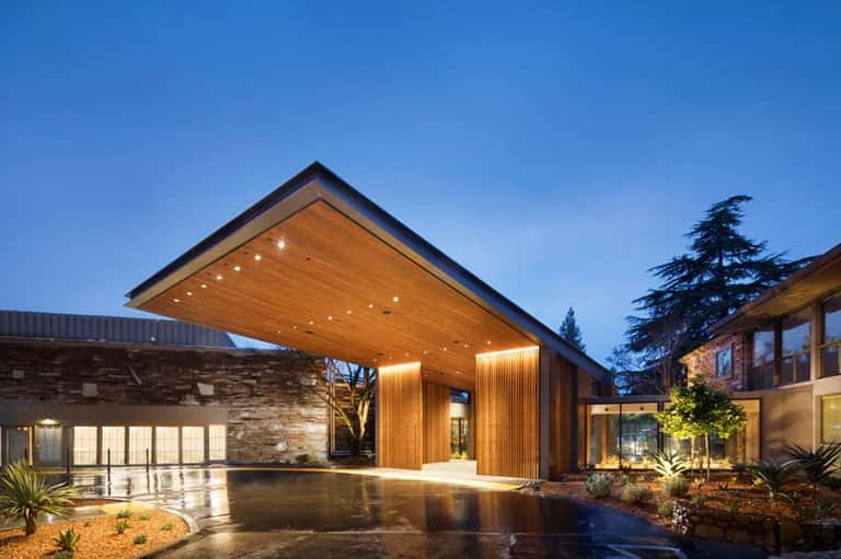 Modern residential courtyard with wooden canopy, stone walls, and uplighting at twilight