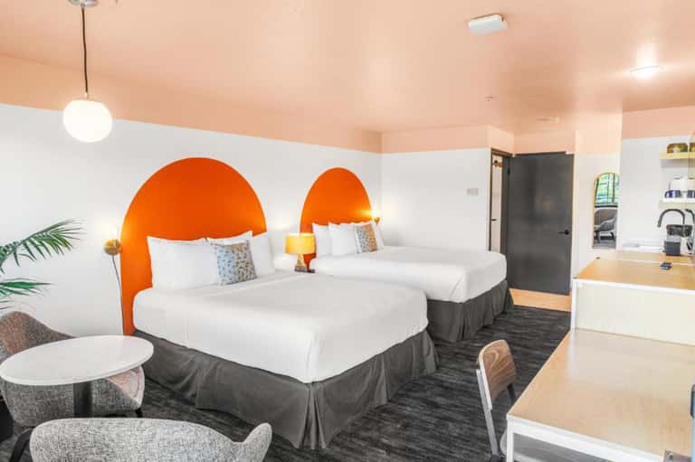 Contemporary hotel room with two queen beds, bold orange headboards, white bedding, and modern furnishings