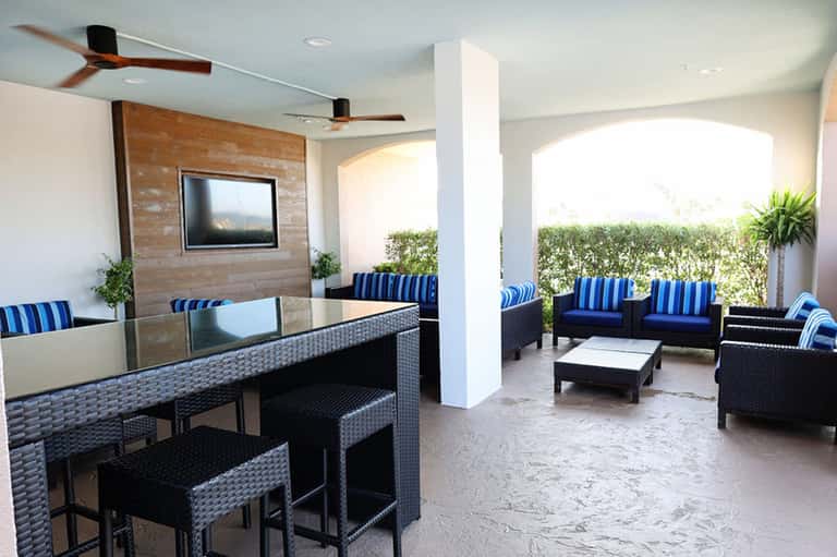 Outdoor terrace with bar seating, dark wicker furniture, blue striped cushions, and ocean views