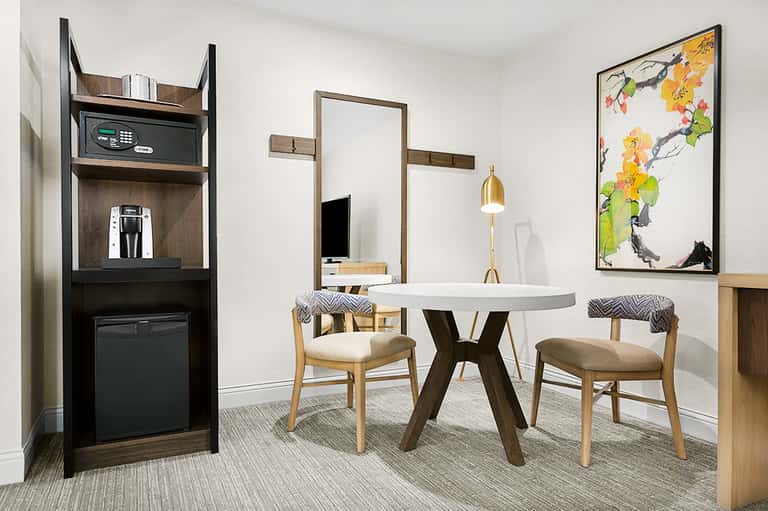 Modern suite interior with round dining table, chairs, wall-mounted mirror, and amenities