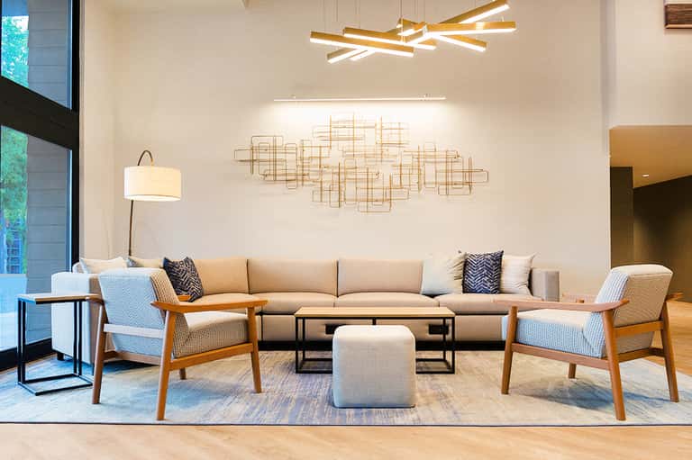 Modern hotel lobby lounge with beige sofa, wooden chairs, geometric wall art, and contemporary lighting