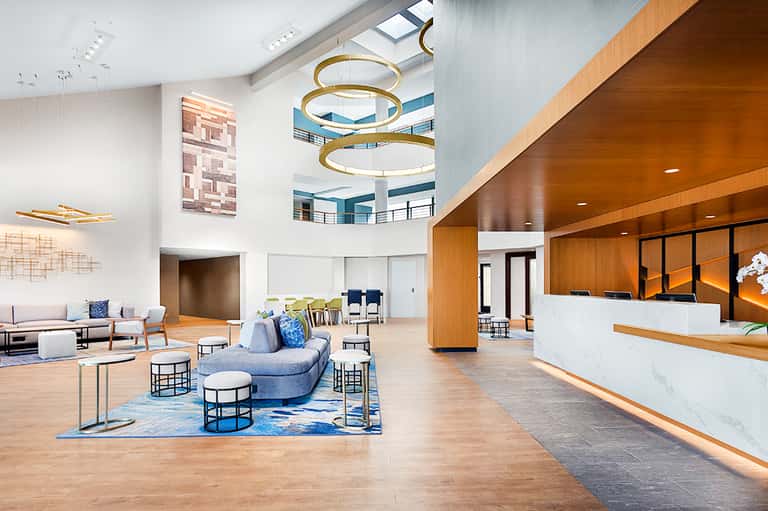 Modern hotel atrium with circular gold chandelier, curved blue sofa, and multi-level architecture