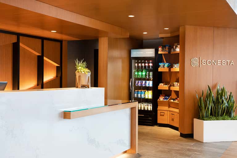 Hotel reception desk with marble counter, warm wood paneling, beverage cooler, and modern minimalist design.