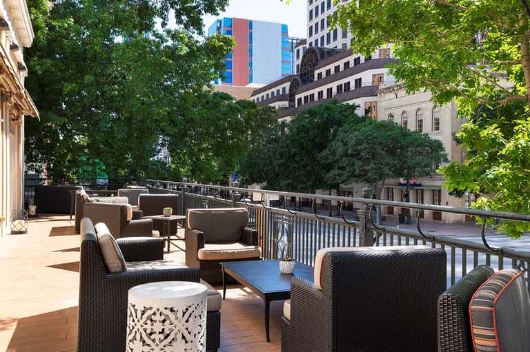 Urban rooftop lounge with brown wicker seating, city skyline views, lush green trees, and modern architecture