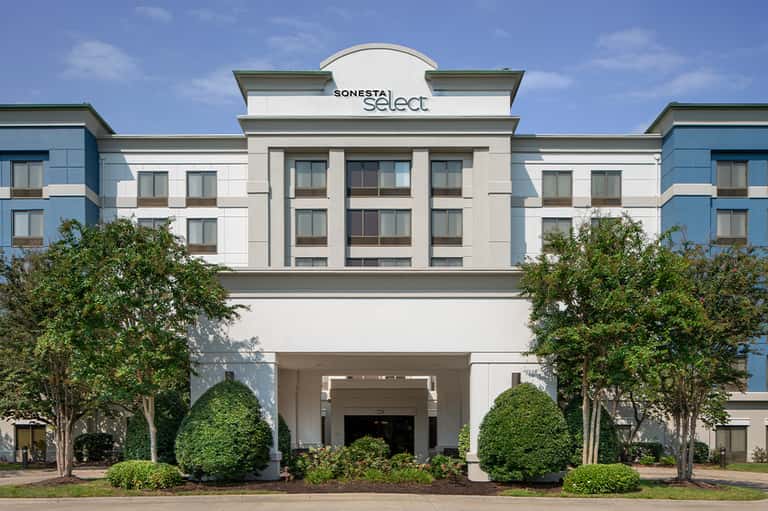 Sonesta Select hotel exterior featuring white facade, green landscaping, and contemporary architecture