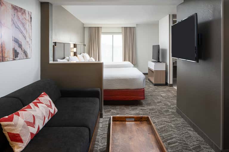 Modern hotel room with queen beds, dark sofa, TV, and neutral contemporary furnishings